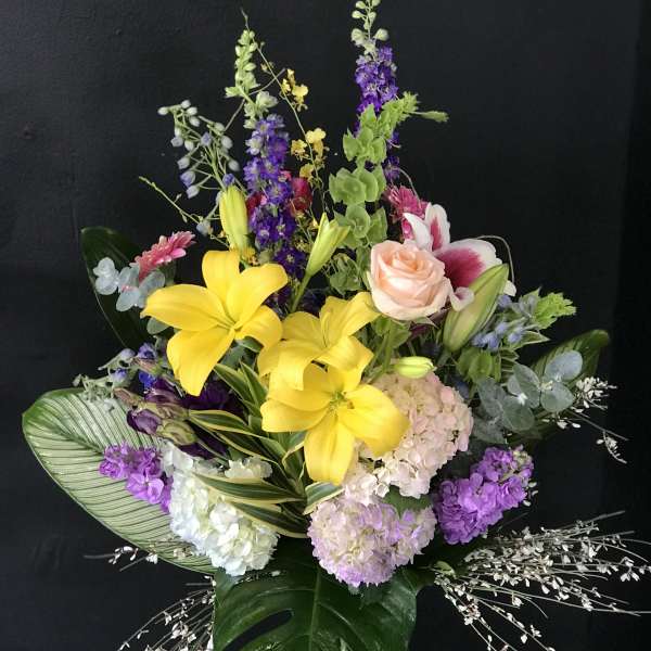 Tall mixed bouquet with yellow lilies, pink roses, and purple flowers in a glass vase