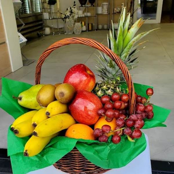 Wicker basket filled with assorted fresh fruit including bananas, apples, grapes, and a pineapple.