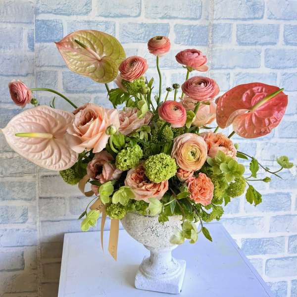 Pink and peach floral arrangement in a white pedestal vase