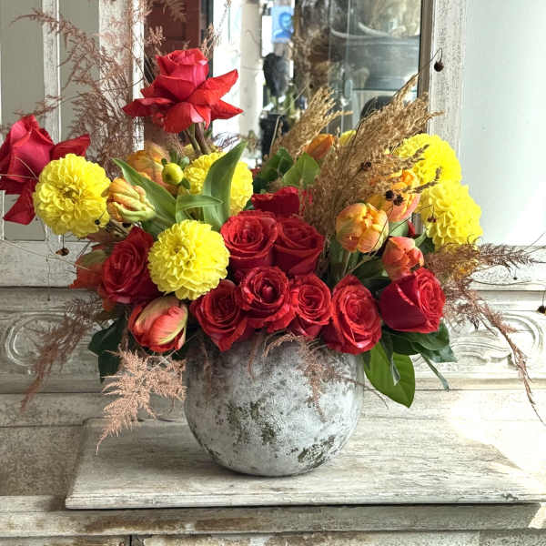Red roses and yellow pom flowers arranged in a gray vase