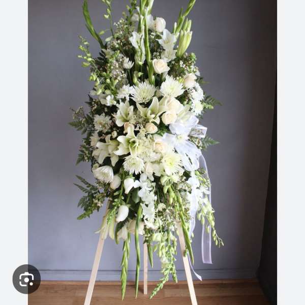 Tall white floral standing spray on an easel with ribbon