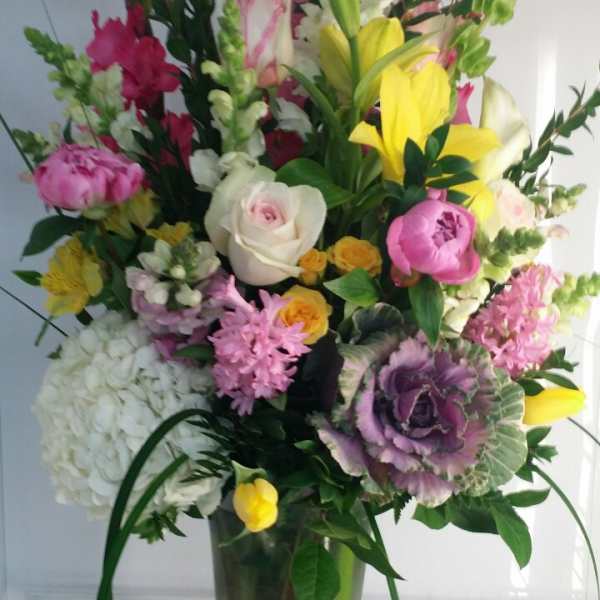 Tall mixed bouquet in a clear glass vase with pink, yellow, white, and purple flowers