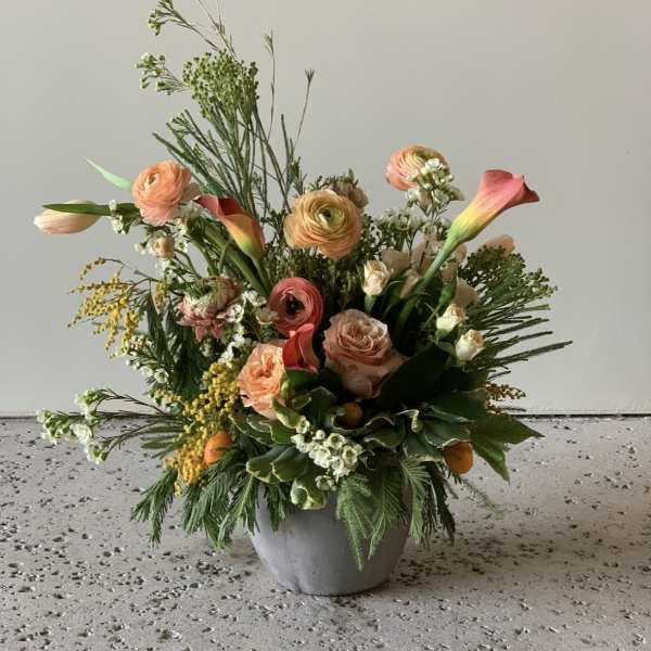 Mixed peach and coral flowers arranged in a gray pot