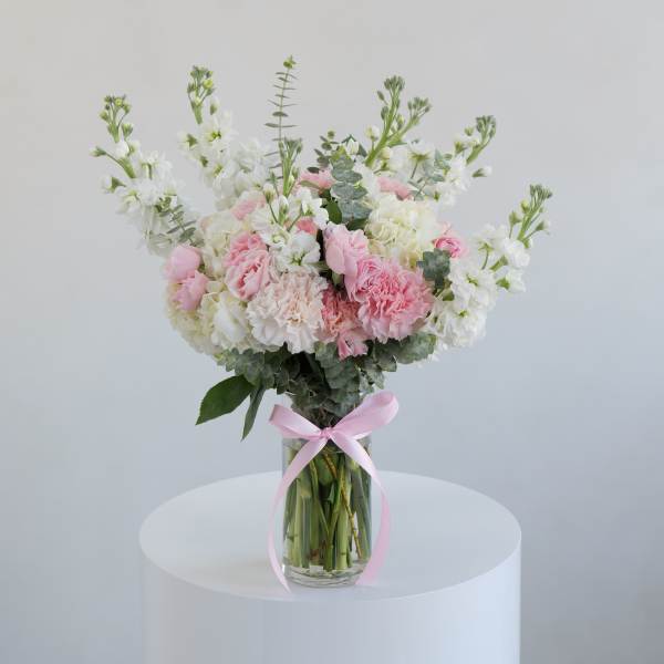 Pink and white bouquet in a clear glass vase with a pink ribbon