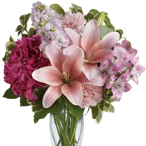 Pink lilies and mixed blooms arranged in a clear glass vase