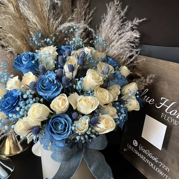 Blue and cream roses arranged in a white hatbox with a ribbon.