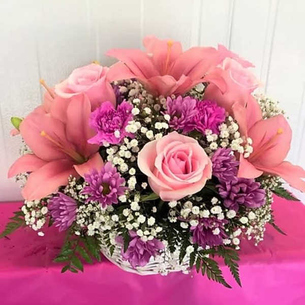 Pink lilies and roses in a white basket with purple filler flowers