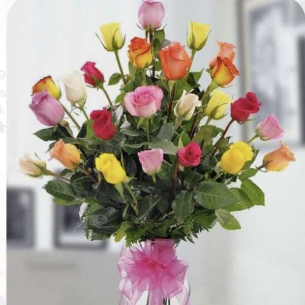 Tall bouquet of multicolored roses in a clear vase with a pink ribbon