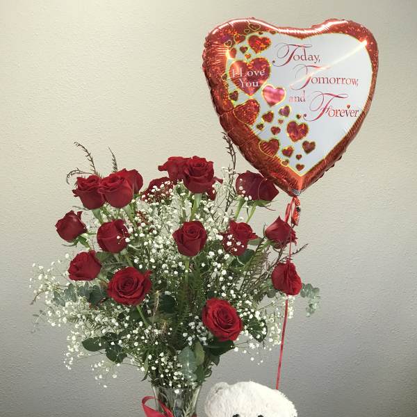 Red roses in a glass vase with a heart balloon and teddy bear