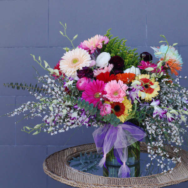 Colorful mixed bouquet in a glass vase with a purple ribbon