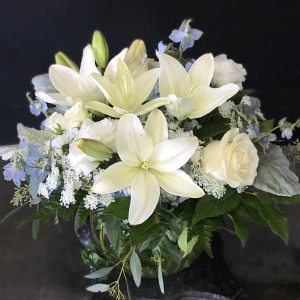 White lilies and roses arranged with pale blue flowers in a vase