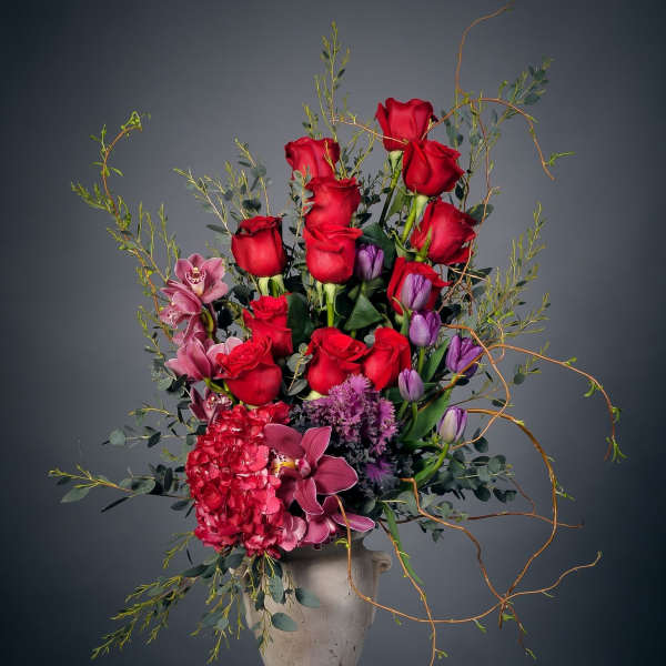 Tall bouquet of red roses, purple tulips, and pink orchids in a stone vase