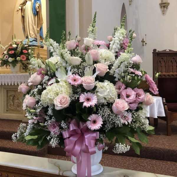 Large pink and white floral arrangement in a church with a ribboned vase