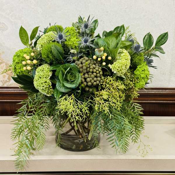 Green floral arrangement in a glass vase with trailing foliage