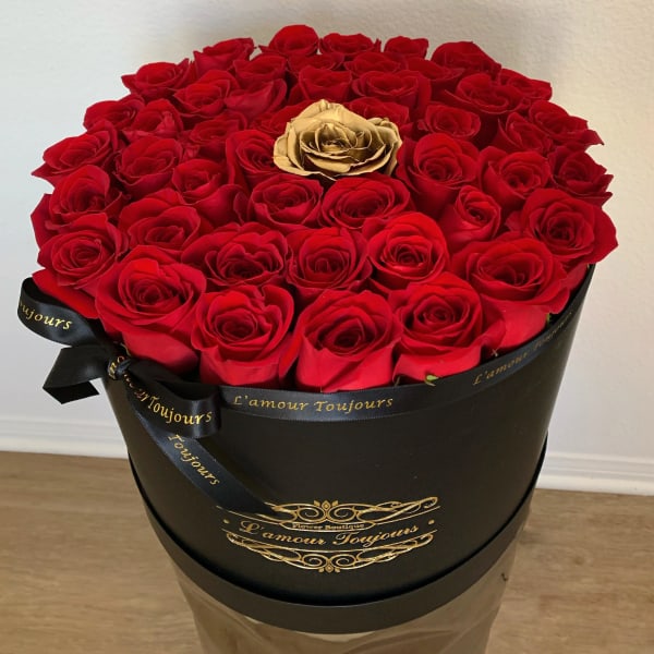 Round black hatbox filled with red roses and a single gold rose in the center