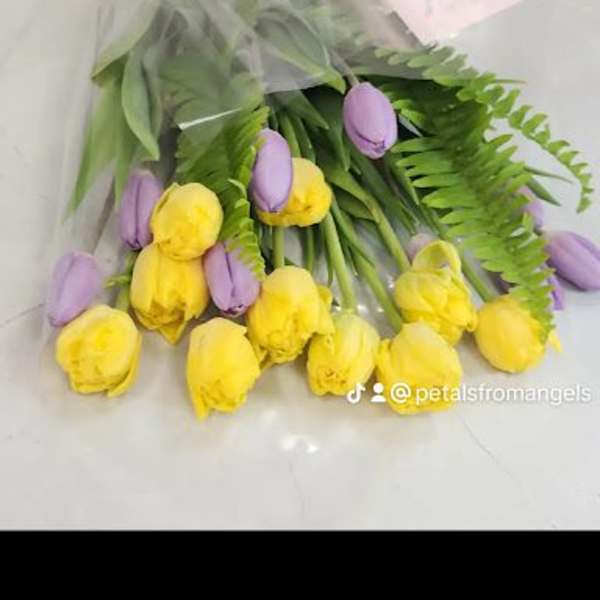 Wrapped bouquet of yellow and lavender tulips with fern fronds and a yellow ribbon