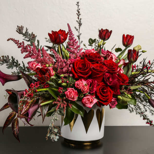 Red roses and tulips in a white vase with dark foliage