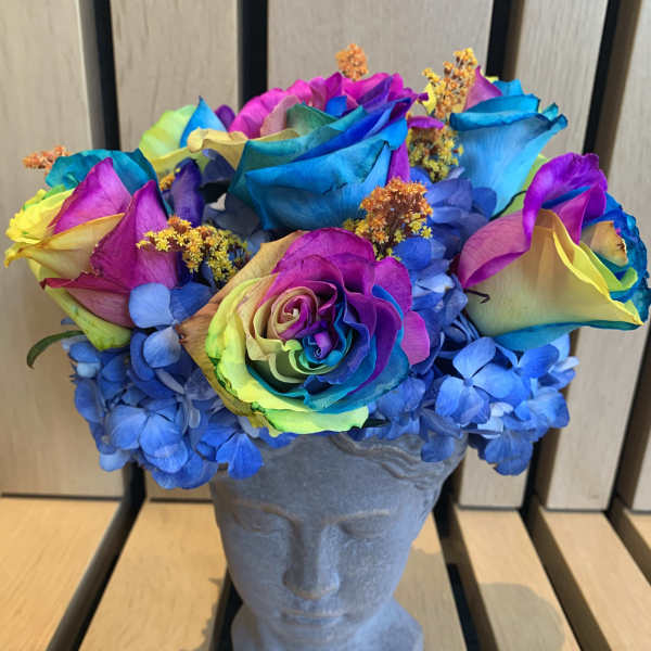 Rainbow-colored roses and blue hydrangeas in a gray bust vase