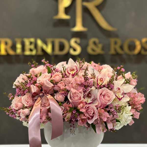 Pink roses and orchids arranged in a white vase with a satin ribbon