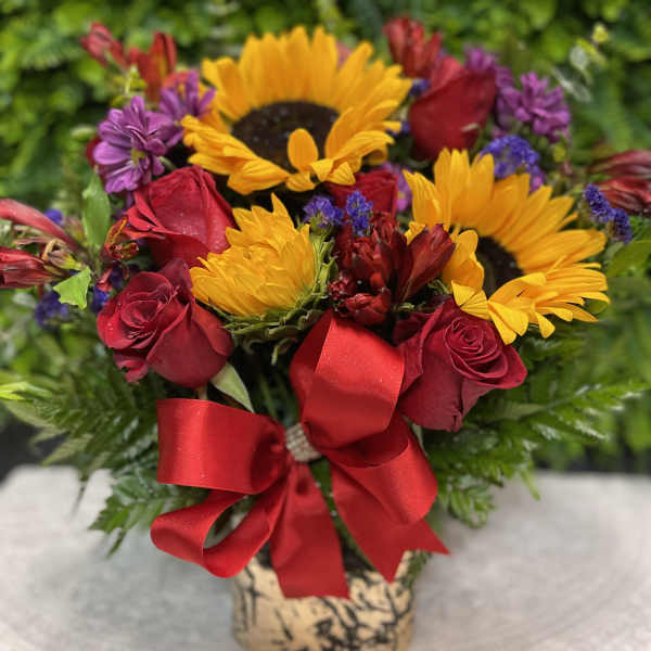 Bouquet of red roses and yellow sunflowers with a red ribbon in a vase