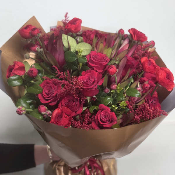 Bouquet of red roses and burgundy flowers wrapped in brown paper