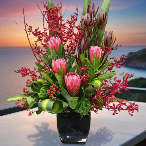 Pink protea arrangement in a black vase with red accents