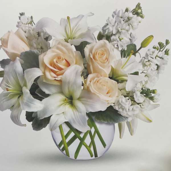 Cream roses and white lilies in a round glass vase