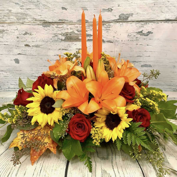 Orange lilies and red roses with sunflowers in a low arrangement.