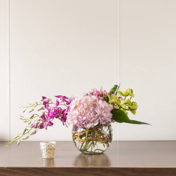 Pink and green orchid arrangement in a round glass vase with a small candle nearby