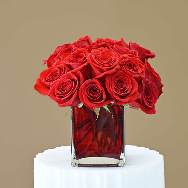 Red roses arranged in a square glass vase with red water