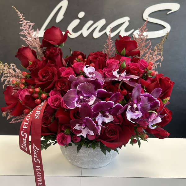 Red roses and purple orchids in a round gray vase with a ribbon