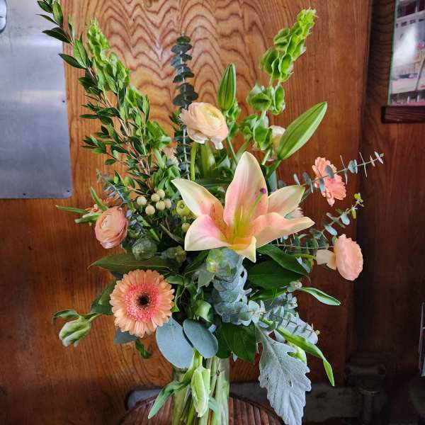 Mixed bouquet with a pink lily, peach gerbera daisy, and pale roses in a glass vase