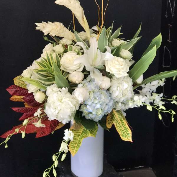 White floral arrangement in a tall vase with tropical leaves and branches