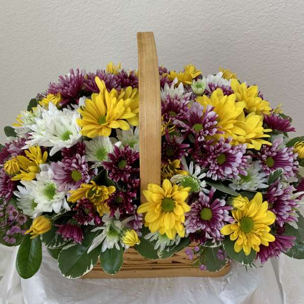Basket of yellow, white, and purple daisy flowers with a wooden handle
