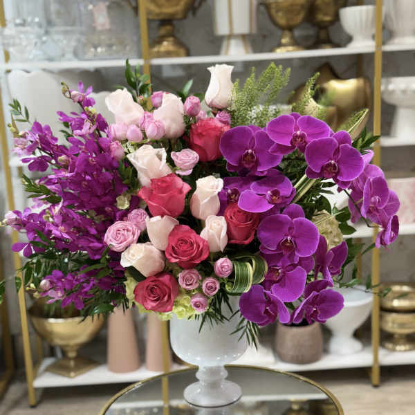 Pink and purple floral arrangement in a white pedestal vase