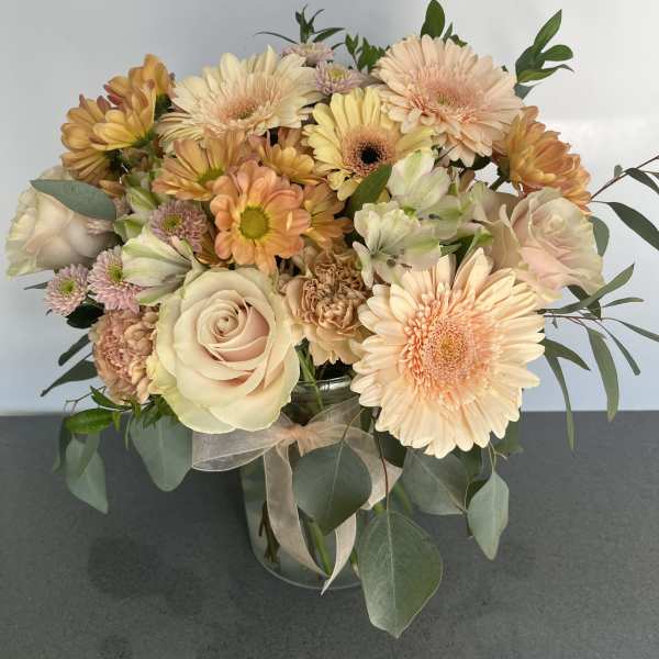 Peach and cream bouquet of roses, gerbera daisies, and carnations in a glass vase