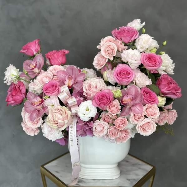 Pink and white roses with orchids arranged in a white vase