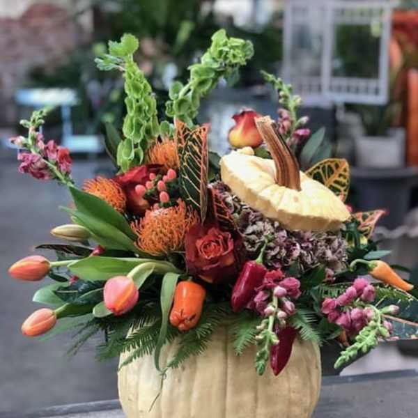 Autumn floral arrangement in a pumpkin-shaped container with roses and tulips
