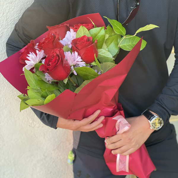 Bouquet of red roses and pale purple daisies wrapped in pink paper