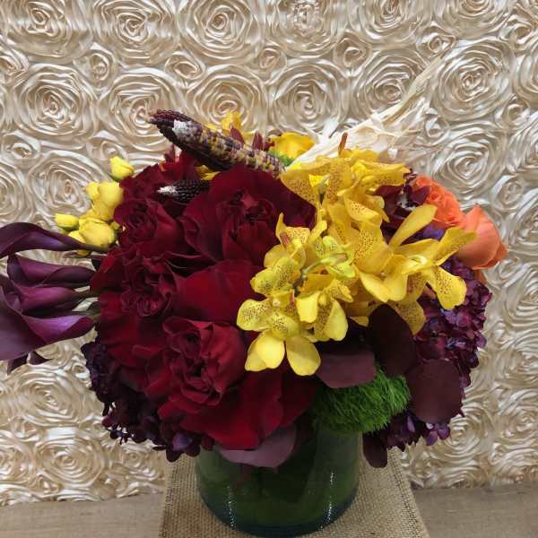 Bouquet of red roses, yellow orchids, and purple calla lilies in a glass vase