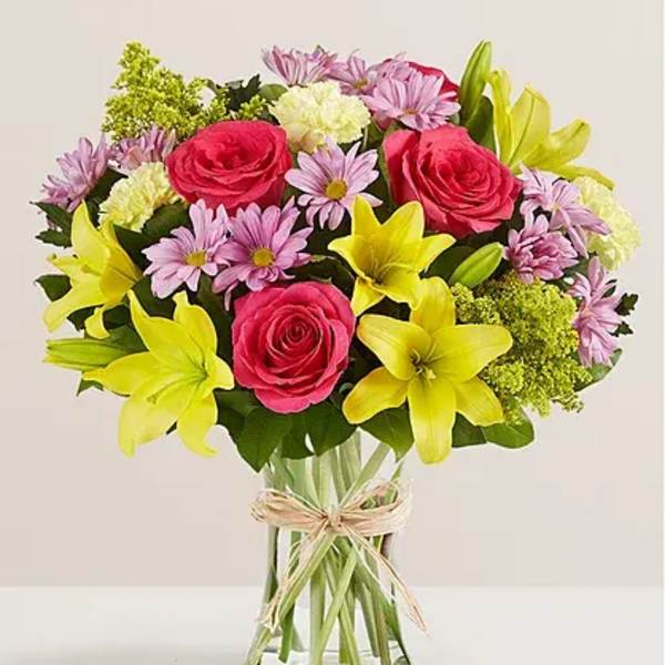 Bouquet of pink roses, yellow lilies, and lavender daisies in a glass vase