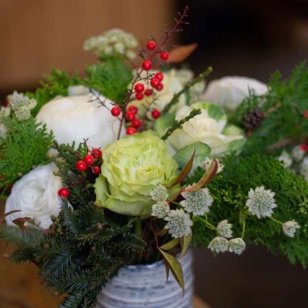 White and pale green floral arrangement in a white vase with red berry accents