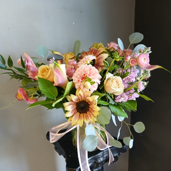 Mixed bouquet with sunflowers, roses, calla lilies, and a pink ribbon in a vase