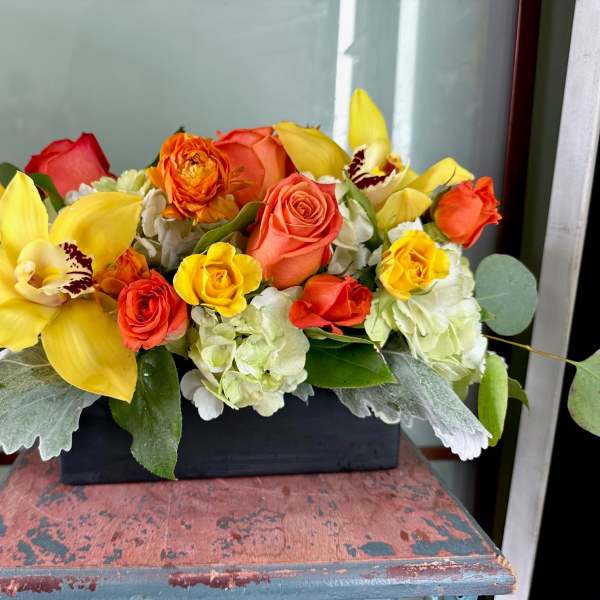 Yellow orchids and orange roses in a black rectangular container