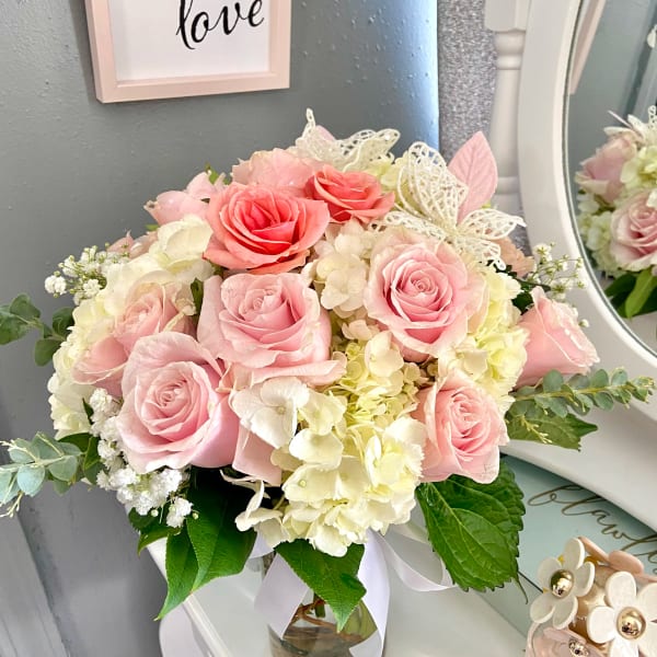 Pink roses and white hydrangeas arranged in a glass vase with a ribbon.