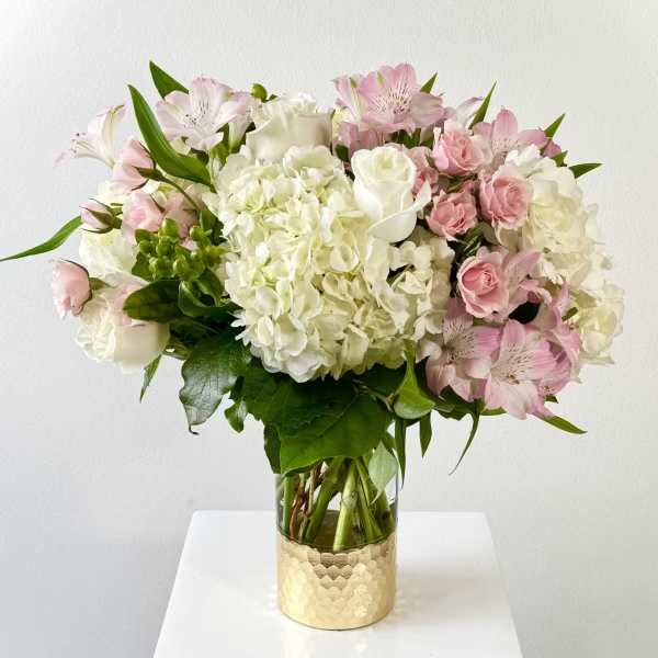 Pink and white bouquet in a glass vase with a gold base