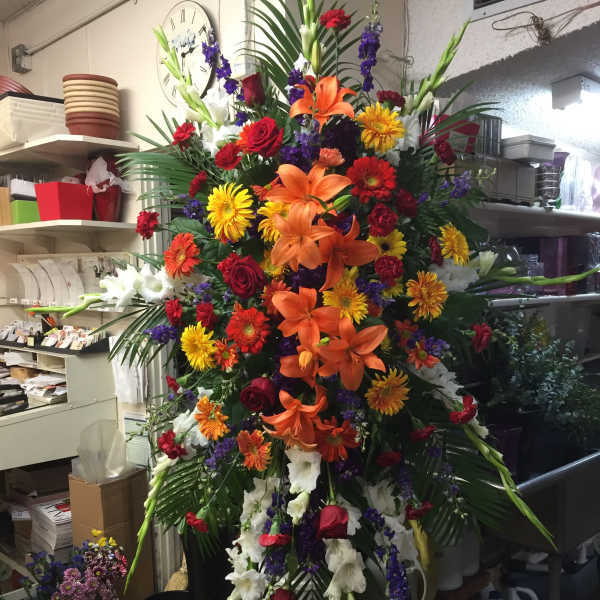Large standing floral spray with lilies, roses, and daisies in bright mixed colors