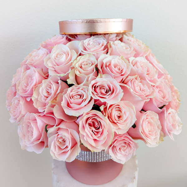 Pink roses arranged in a round hatbox with a satin lid and rhinestone band