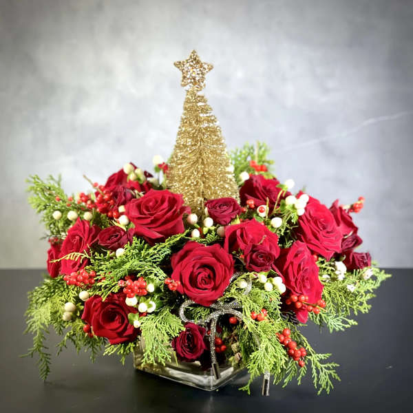 Red roses arranged around a gold tree topper in a glass vase