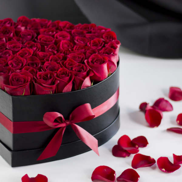 Heart-shaped box filled with red roses and scattered rose petals